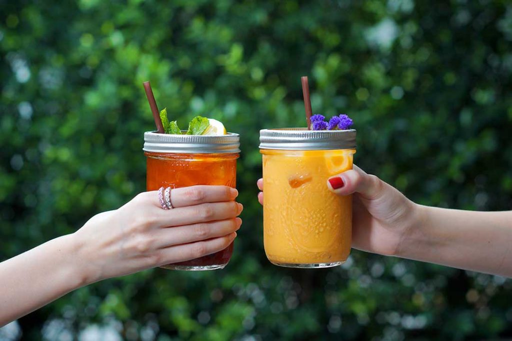 How to Cold Brew Tea—Image shows two hands holding a jar of iced tea and a jar of juice together—cheers!