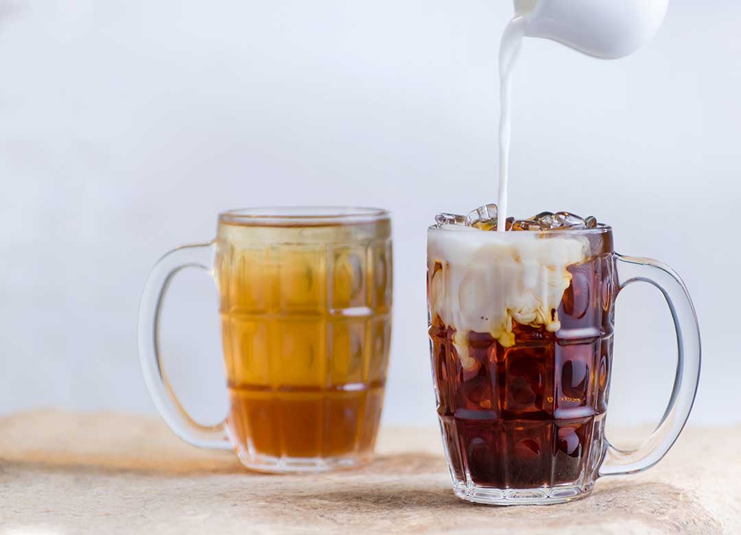 How to Cold Brew tea—Image shows a cup of green tea and a cup of black tea with milk being poured into it.