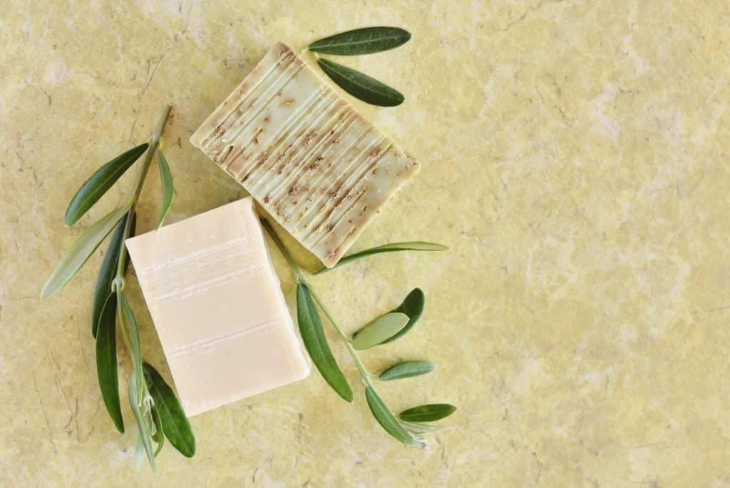 Handmade soap bars and olive branches on color background, top view. (Soap Making Kits for Beginners)