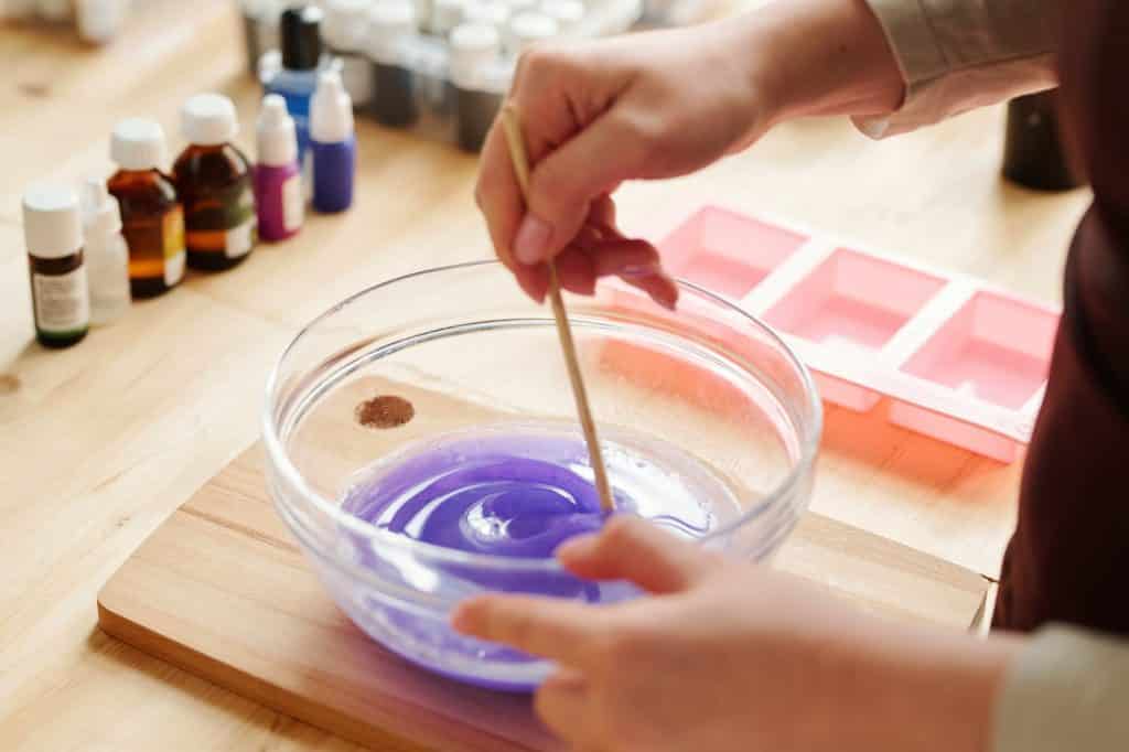 Hands of creative girl mixing lavender color with liquid soap mass in glassware (Soap Making Kits for Beginners)