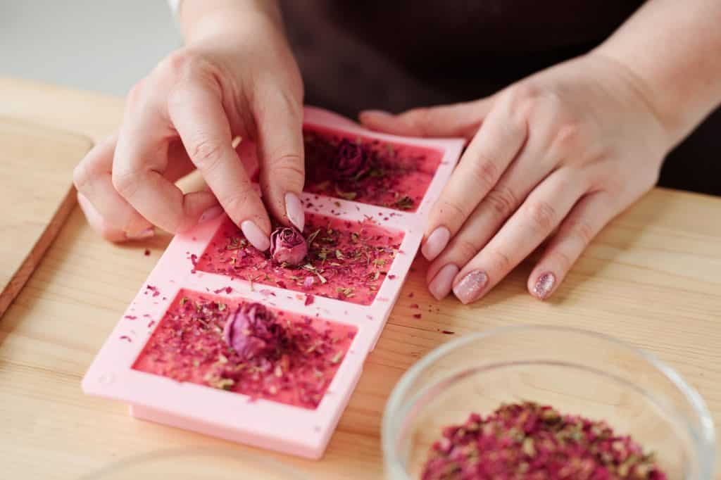 Hands of young woman putting small rosebuds on top of pink soap bars