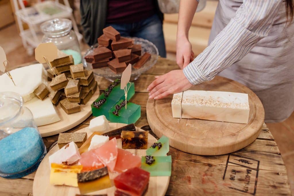 Shop assistant cutting bars of natural soap for customer in package free store. (Soap making kits for beginners)