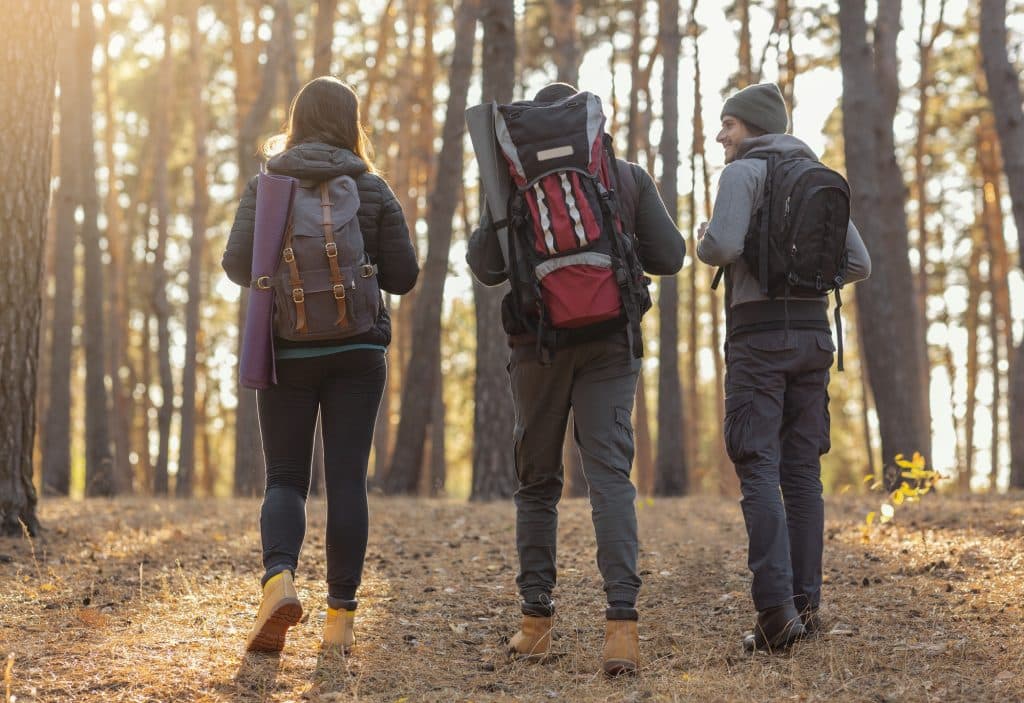 Ready to start hiking? Check out our hiking gear list as well as some resources for finding trails near you before you head out! (Three friends with their backpacks hiking through an autumn forest.)