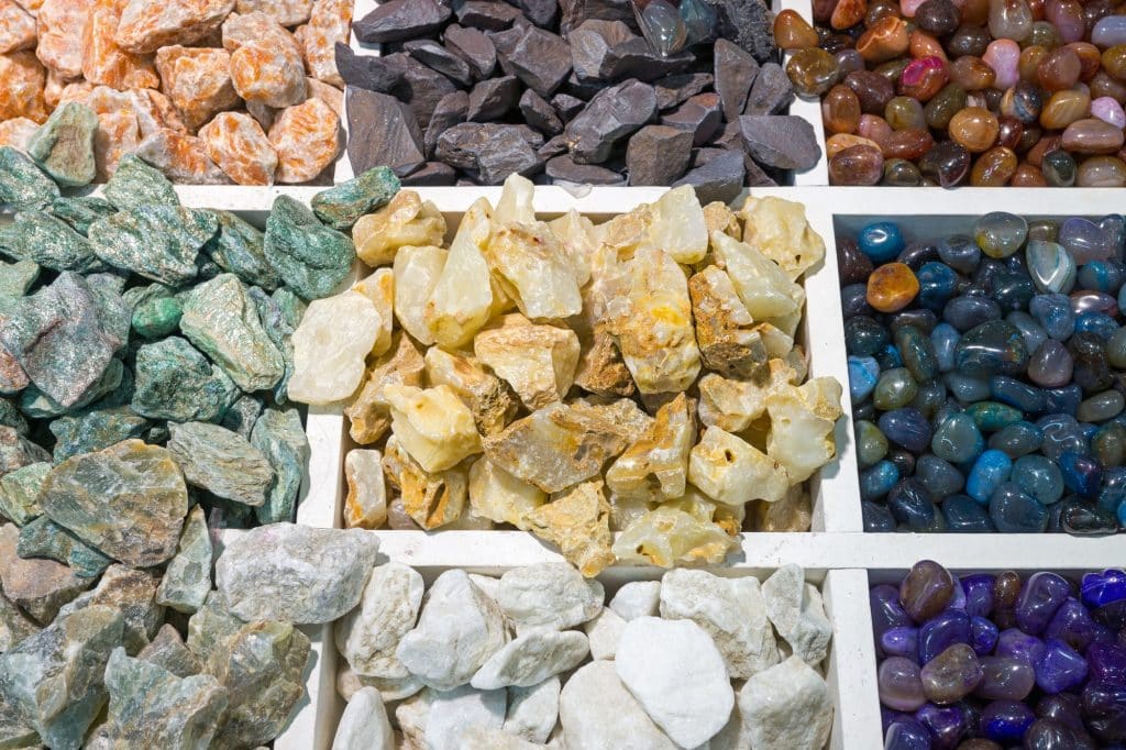 Rock collecting is one of a few hobbies that has the potential to be both rewarding and profitable. Learn more in our rock collecting for beginners guide! (Image shows boxes of colourful semi-precious stones)