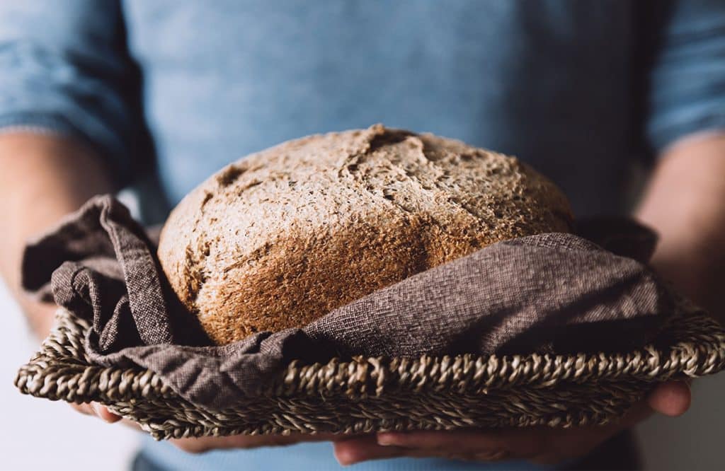 Picture shows a man holding freshly baked bread bread on a wicker tray.