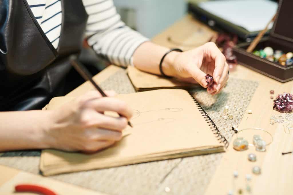 Woman drawing a closeup of earrings, holding a tumbled stone for reference