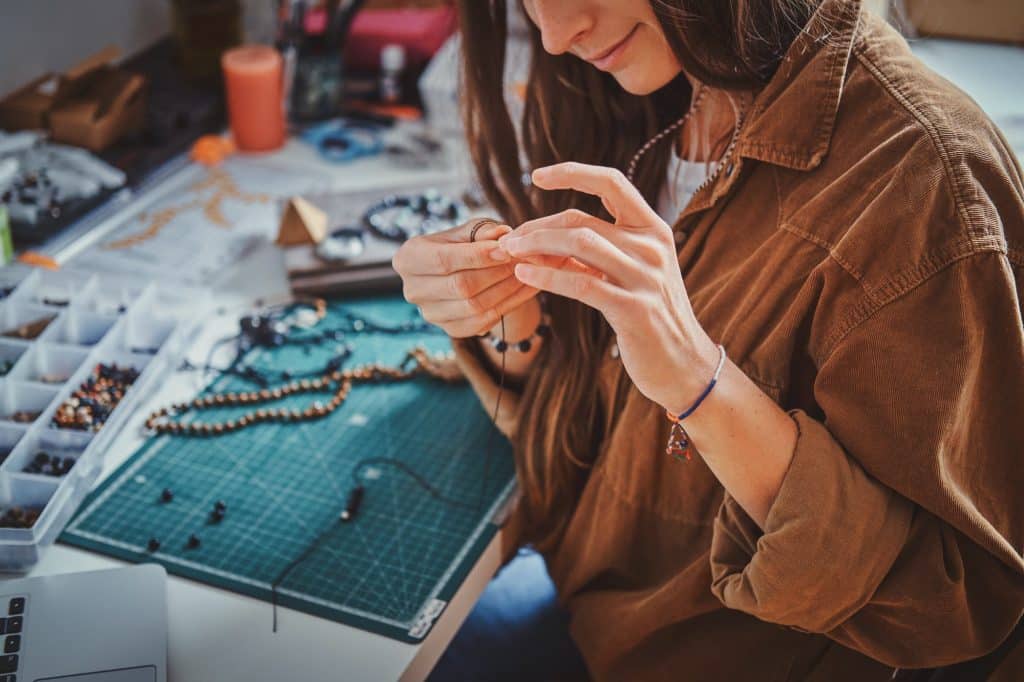 Learn how to make your own tumbled stone jewelry to wear, give as gifts, or sell at your local market days. Here are all the tools you need to get started! (Image shows a girl making new beaded jewelry.)