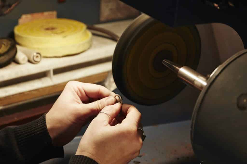 A person holding a small ring and using a grinding machine to shape and polish it. Workbench in a