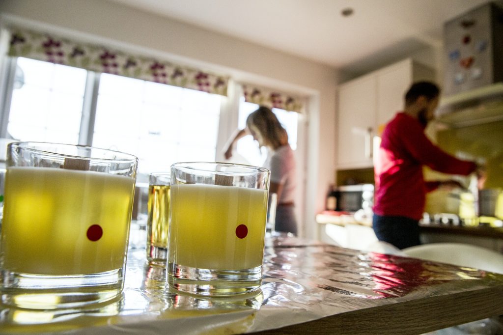 Man and woman standing in a domestic kitchen, making jar candles.