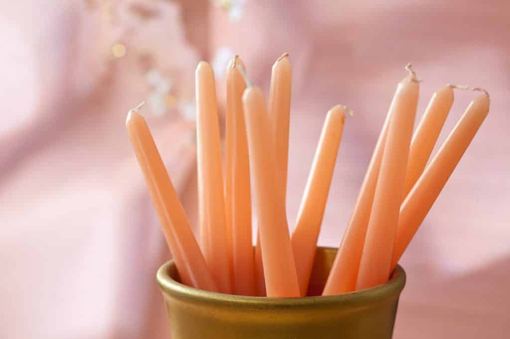 New, white taper candles in a vase against a pink background
