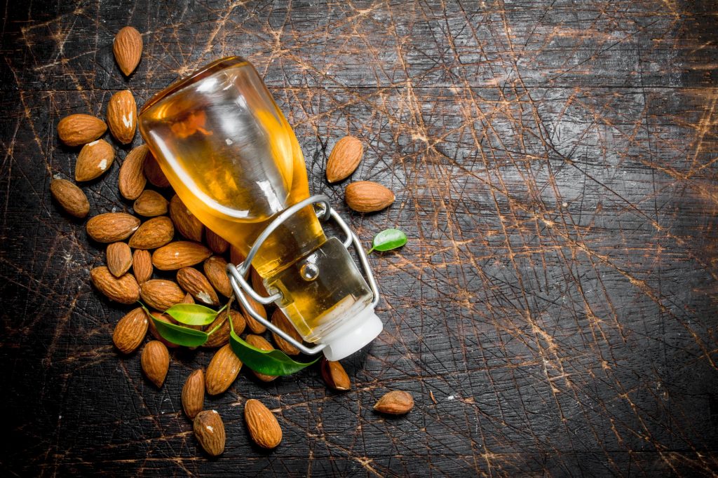 Bottle of almond oil on a dark wooden surface, surrounded by almonds.