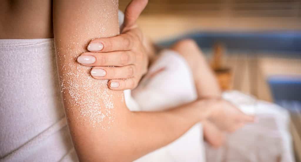 Young woman applying natural scrub sitting in sauna