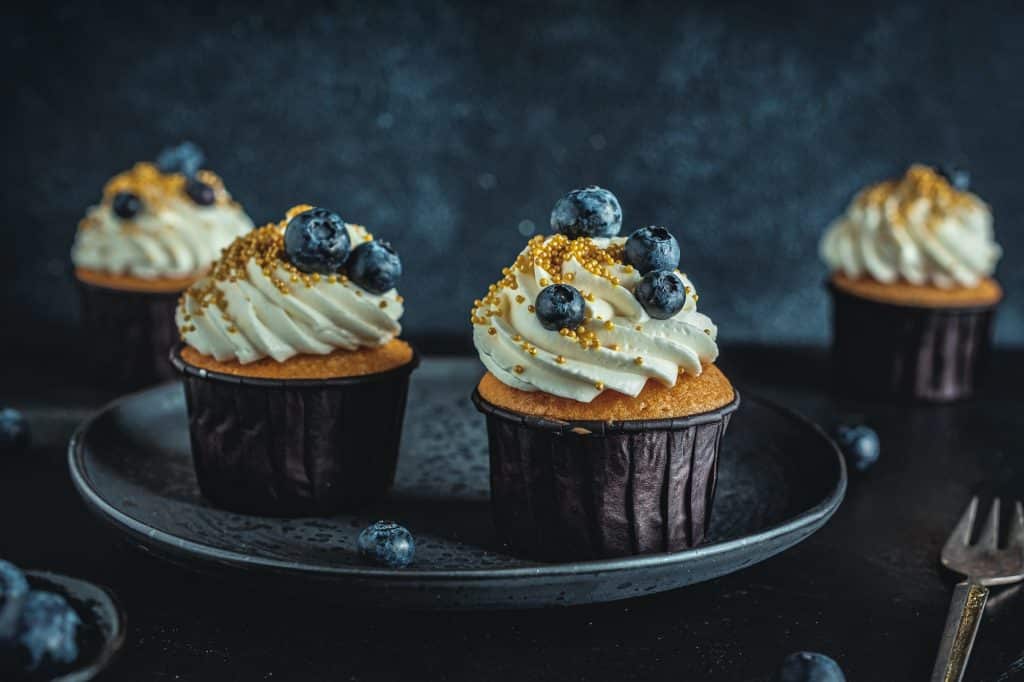 Vanilla cupcakes on plate, topped with blueberries and gold sprinkles