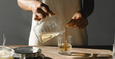 crop black woman pouring wax into candle mold